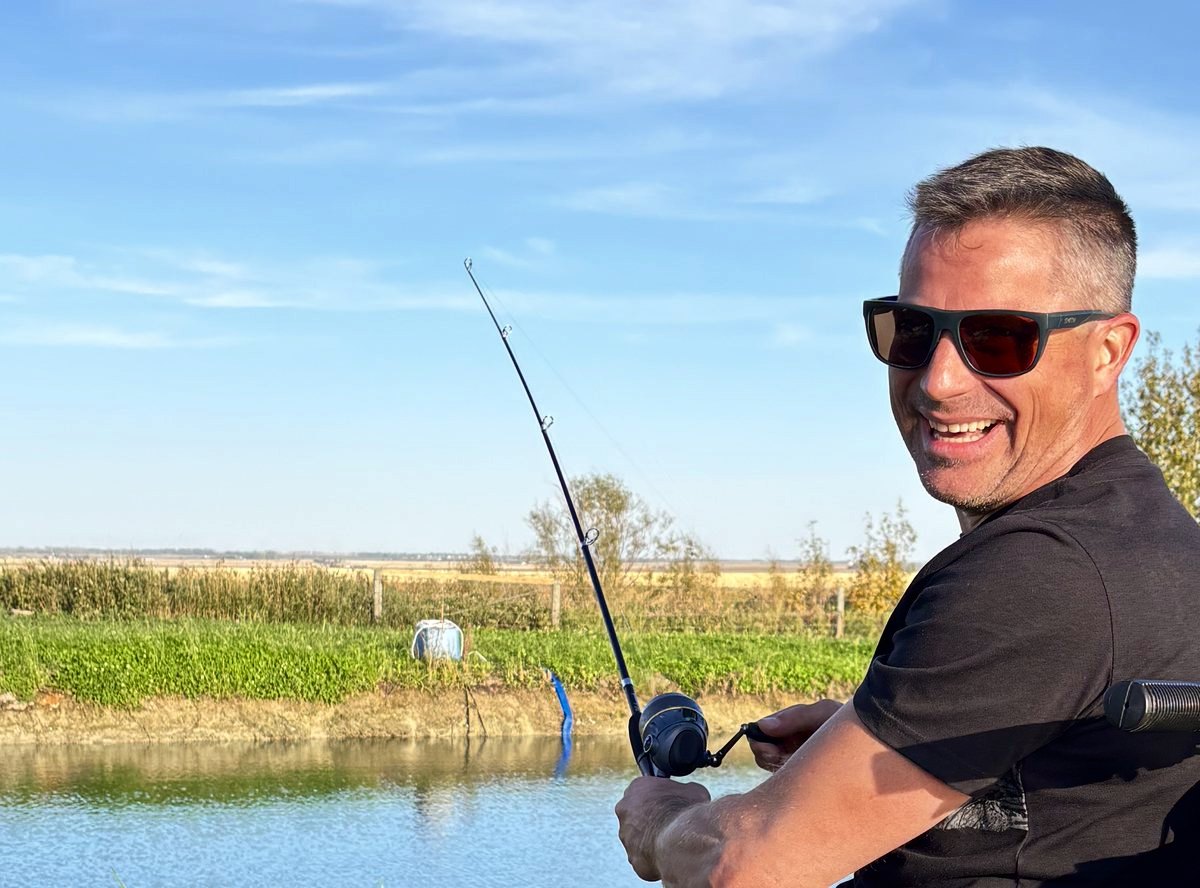An angler grinning over his shoulder with his rod bent toward the pond