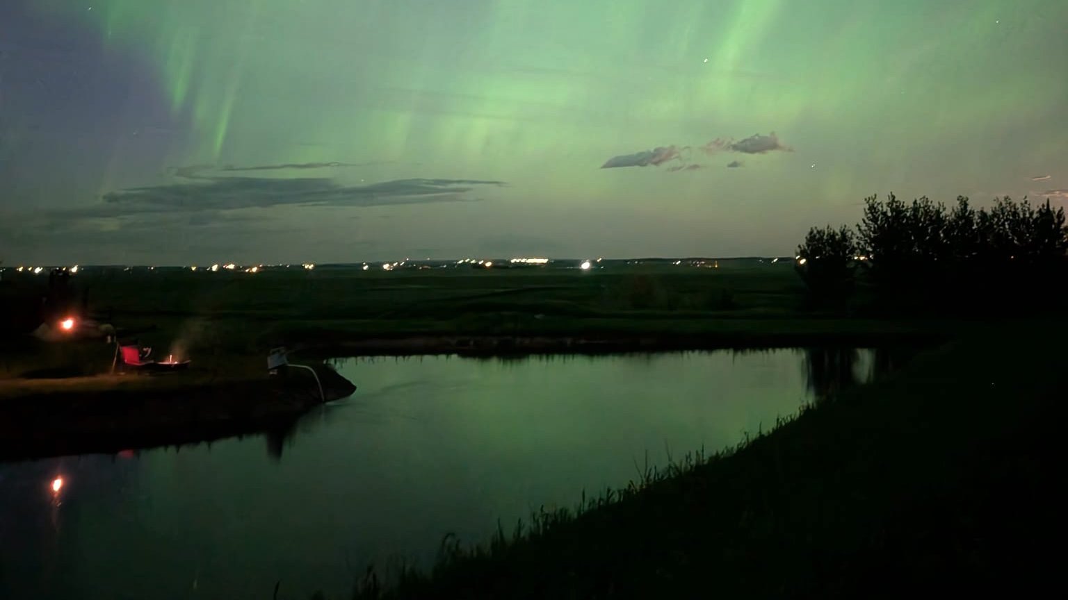 Northern lights over the pond at night, a fire glowing on the bank