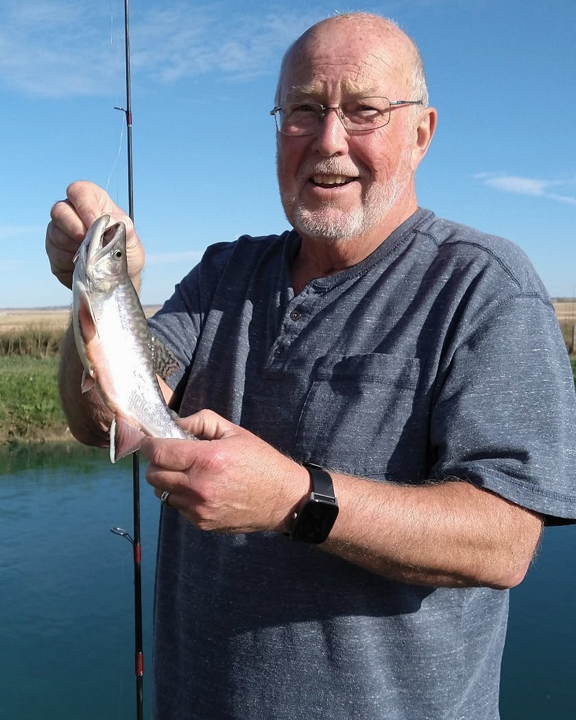 An angler holding up a brook trout beside the pond