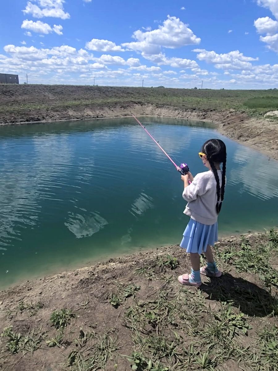 A girl casting with a pink rod under a big summer sky