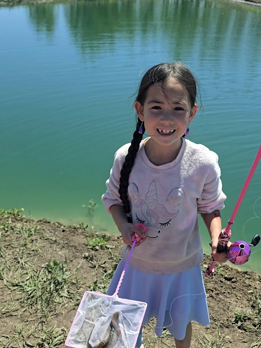 A girl grinning beside the pond with her trout in a pink net