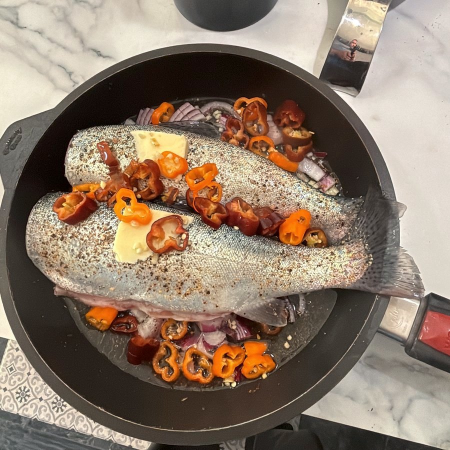 Two whole trout in a cast-iron pan with butter and sliced peppers